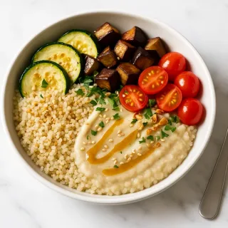 Bowl de fonio pour le déjeuner avec courgettes et aubergines rôties, tomates cerises, sauce tahini-citron en zigzag et graines de sésame grillées