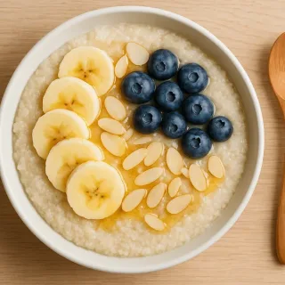 Bol de porridge de fonio crémeux garni de fruits frais et noix, sur fond bois clair